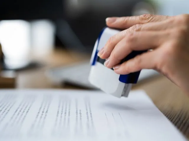 A hand stamping approved permit papers.