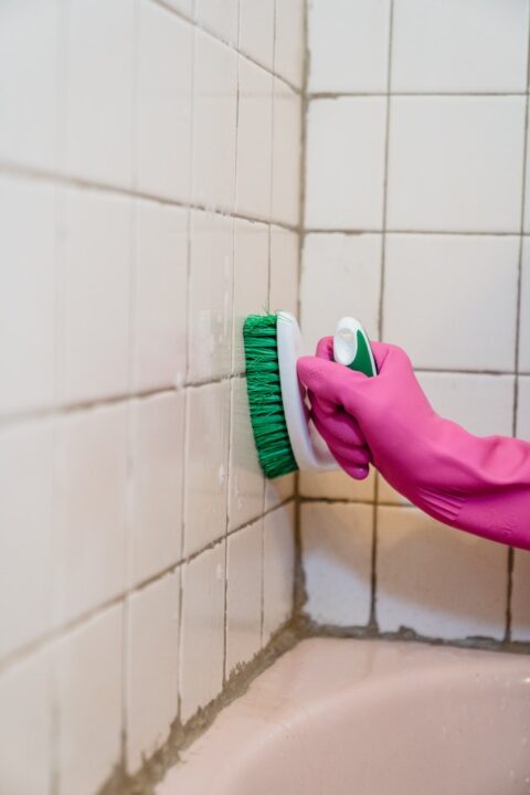 Hand in Rubber Glove Cleaning Bathroom Tiles.