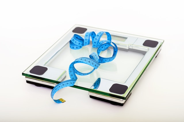 A bathroom scale and tape measure lying on a floor.