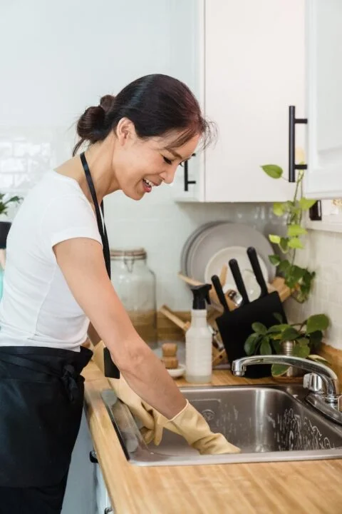 A woman cleaning a sink after washing the dishes.