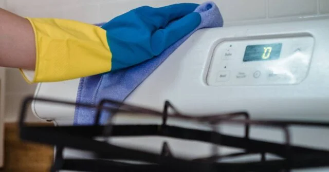 A hand cleaning a stovetop thoroughly.