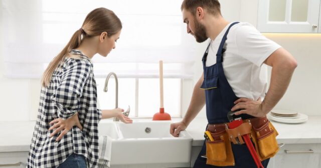 A woman showing the clogged kitchen sink to the plumber.