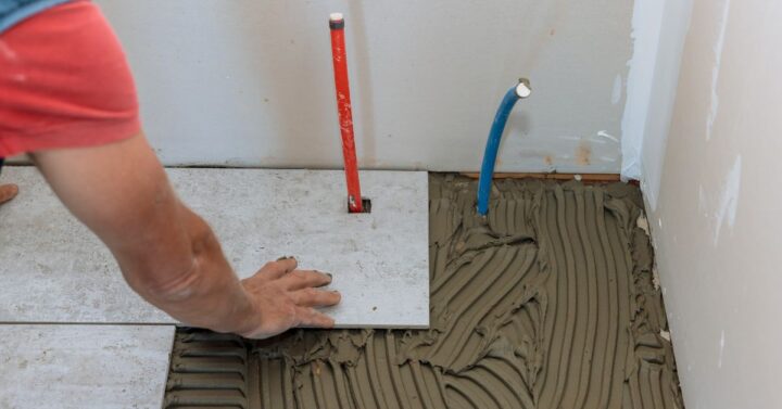 A man carefully installing floor tiles in a bathroom.