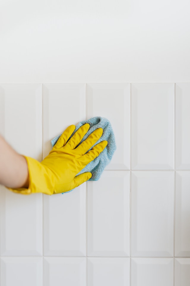 Crop person cleaning white tile wall with microfiber cloth.