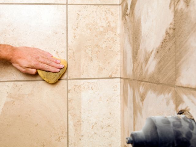 A hand wiping excess grout sealer from initial application.