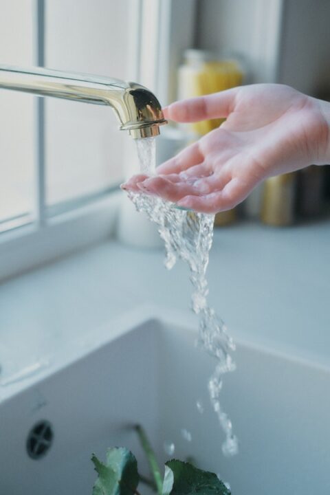 Woman putting her hand under water flowing from the kitchen tap.