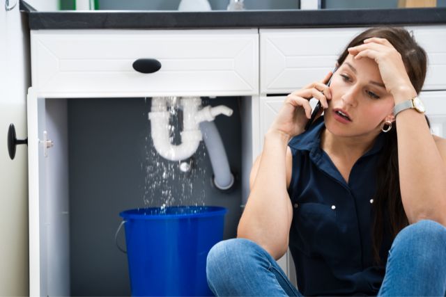 A stressed woman calling someone to repair the sink pipe leak.