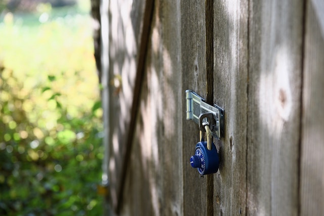 An outdoor storage space locked using a blue combination padlock.