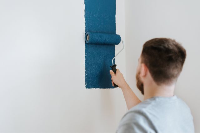 Man painting a wall with a dark blue color.