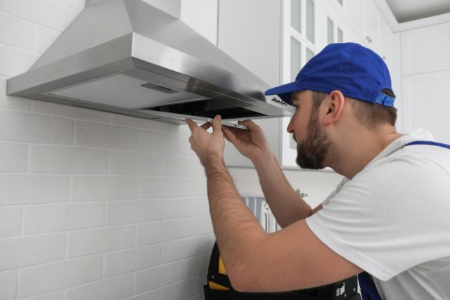 A worker repairing a stove hood of a kitchen.