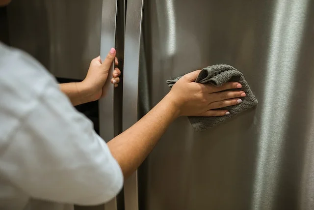 A woman cleaning and wiping the surface of a refrigerator.