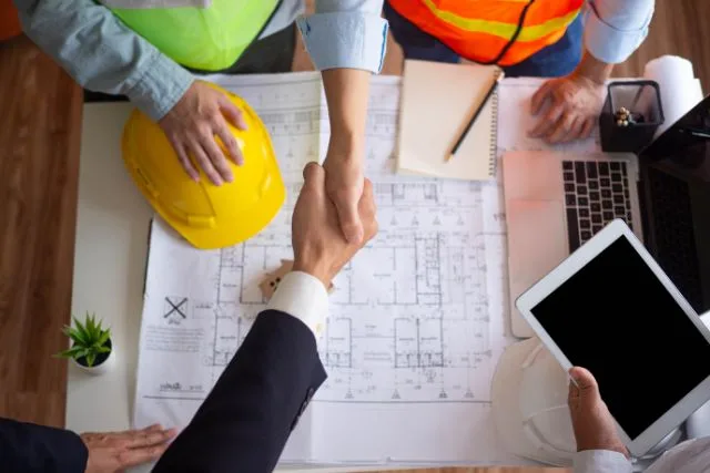 An expert contractor and client shaking hands over renovation blueprint.