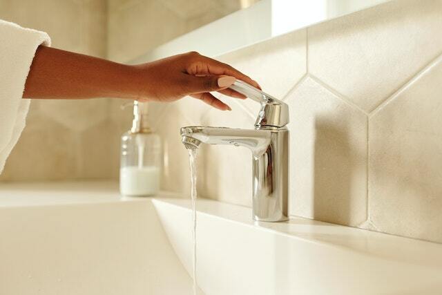 A hand on a bathroom faucet with a running water.