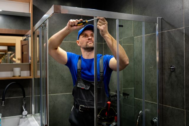 Routine maintenance and repair on a glass shower door by a repairman.