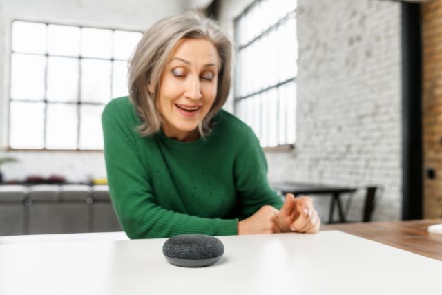 An elderly woman giving voice commands to a smart speaker.