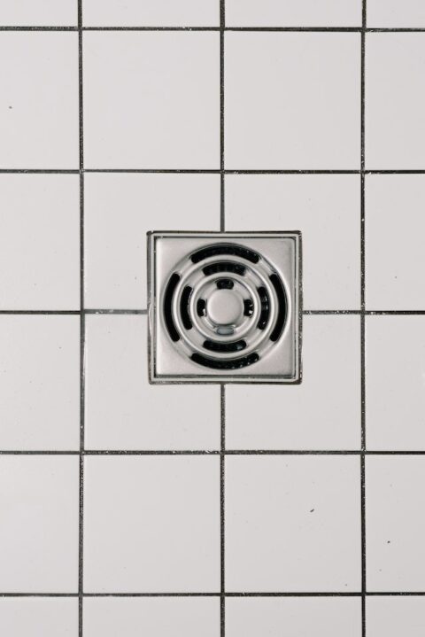 A tiled bathroom floor with stainless steel cover of drain in modern shower.