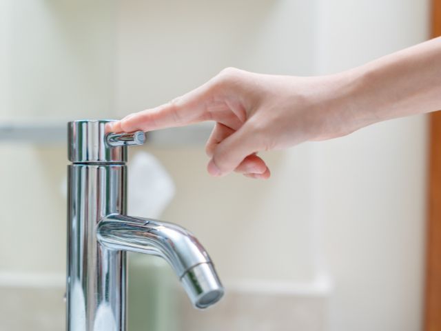 A hand turning off the running water from a bathroom faucet.