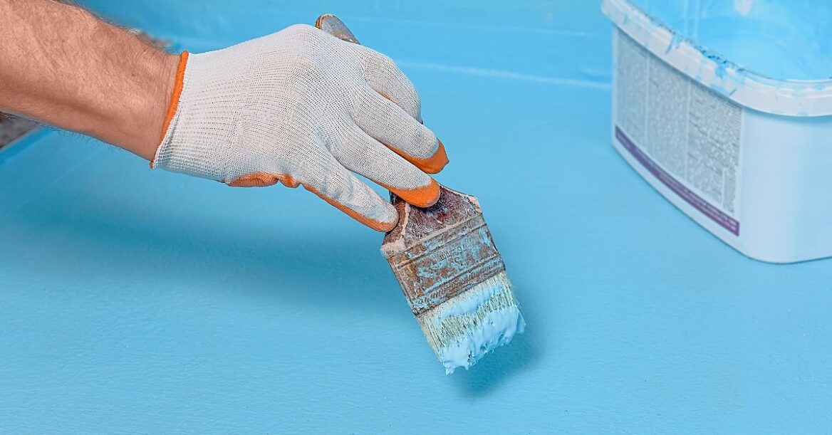 A worker applying waterproofing paint in a batnroom floor.