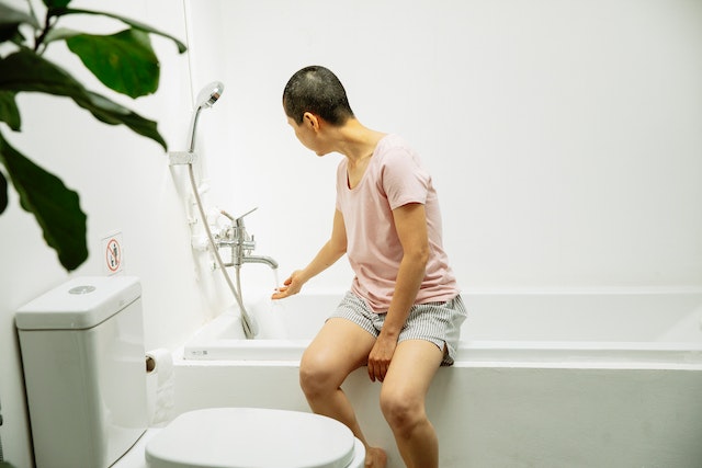 A woman sitting on the bathtub side while checking the water temperature.