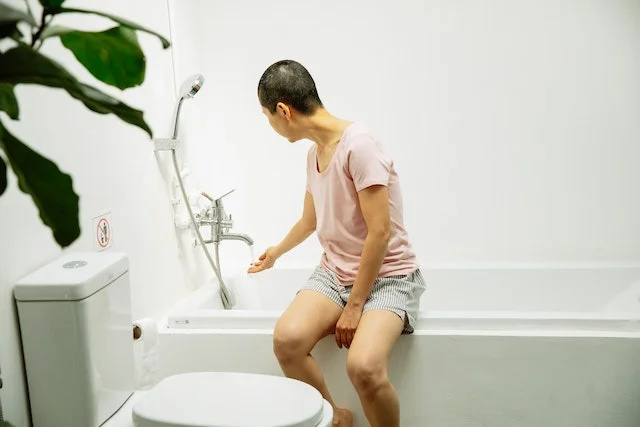 A woman sitting on the bathtub side while checking the water temperature.