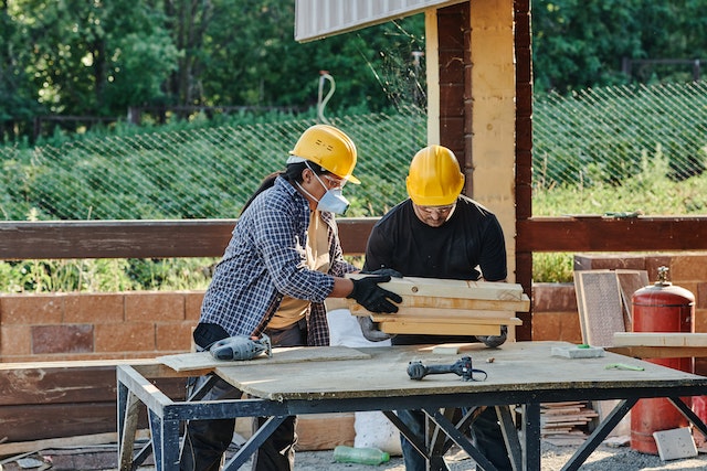 A man and a woman doing wood carpentry wearing complete safety gear.