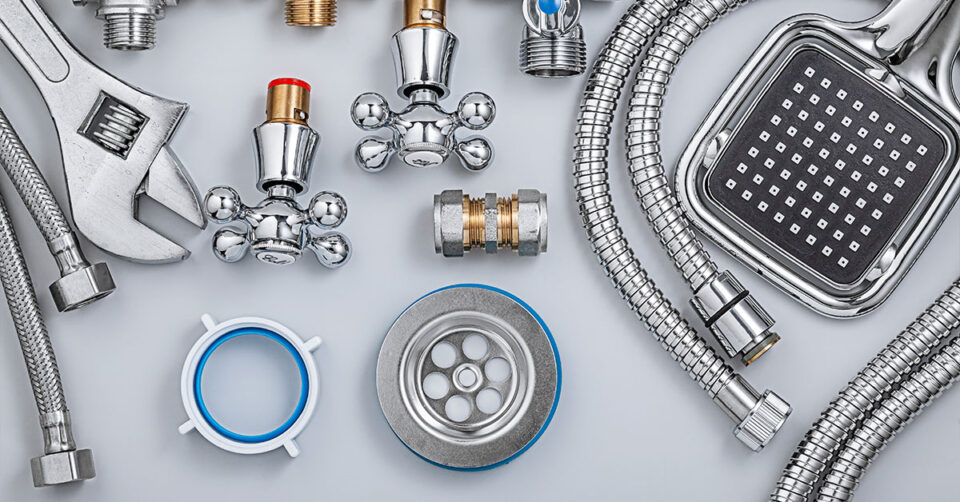 Assorted plumbing tools and fixtures including a wrench, showerhead, hoses, and faucet parts arranged on a flat surface.