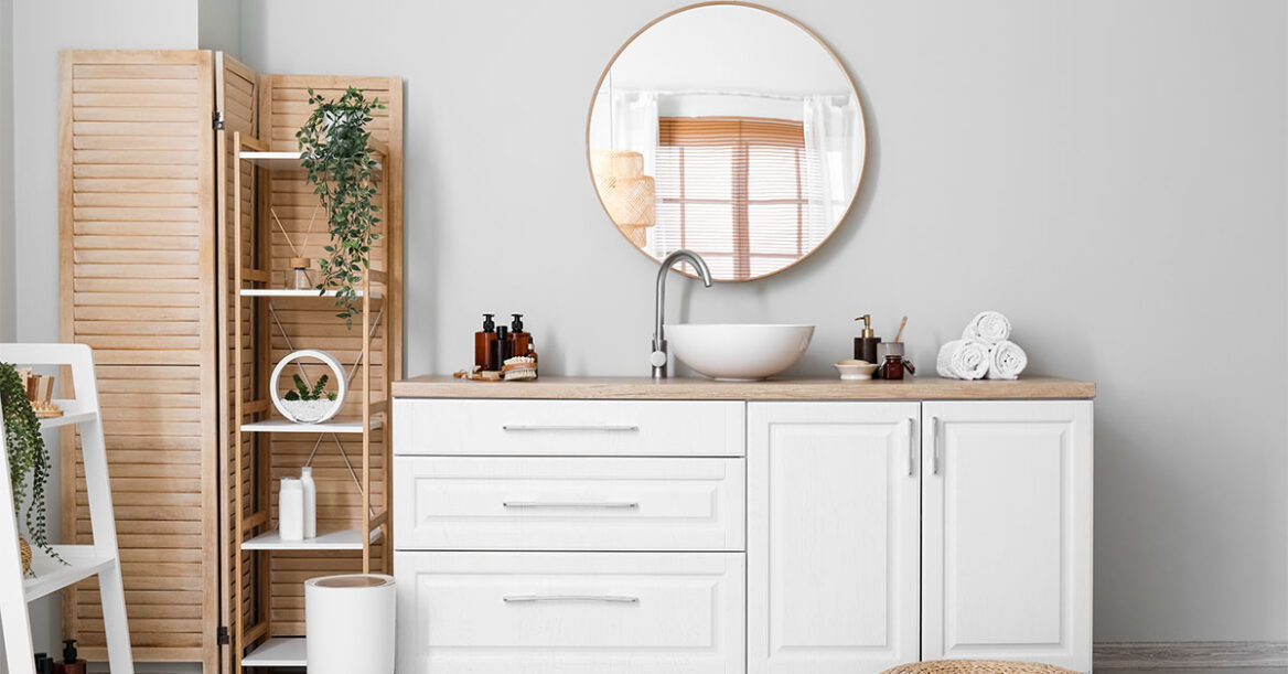 Stylish bathroom with a white vanity, vessel sink, round mirror, natural wood accents, and decorative storage shelves.