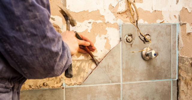 Renovator chiseling tiles off a shower wall.