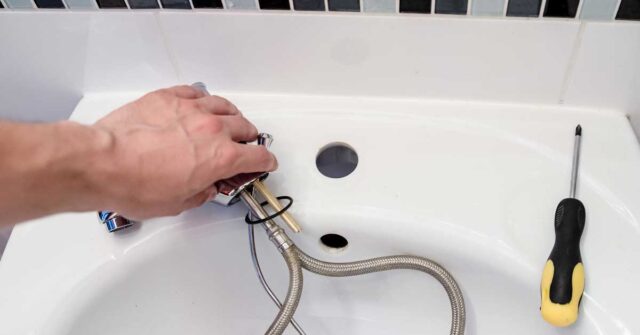 A hand working on a sink faucet.