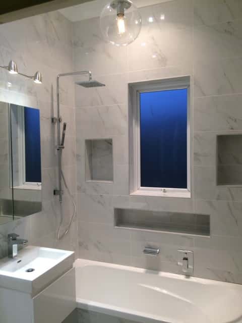 View of entire bathroom. Window is closed and has a blue tinge. Walls are tiled over the bath