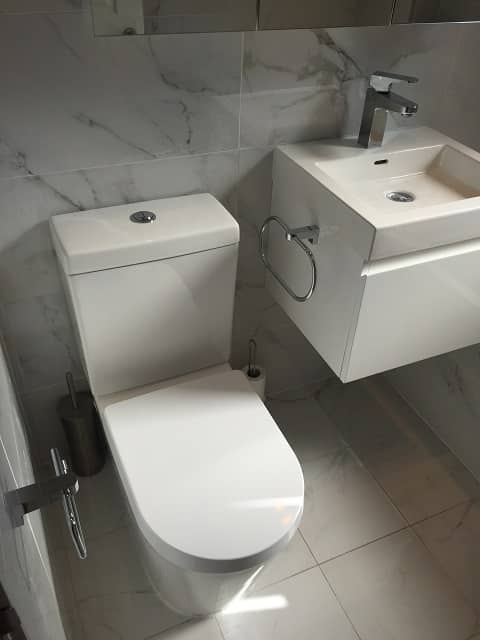 Left view of bathroom with toliet and sink. Tiled walls and floor.