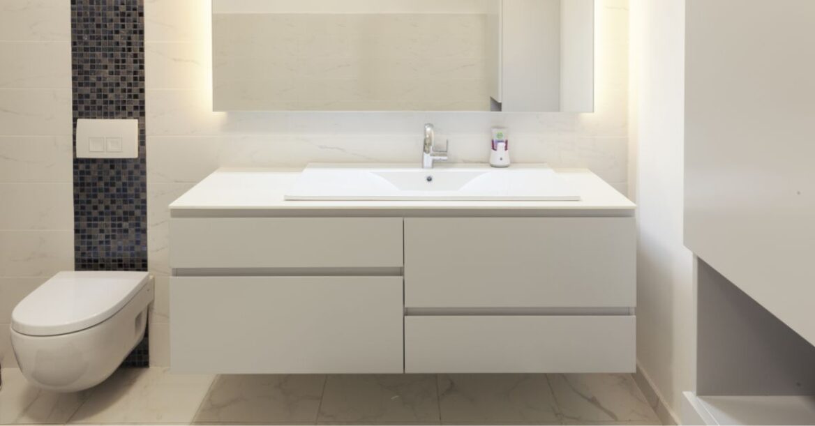 White floating bathroom vanity with large mirror on top and floating toilet to the left.