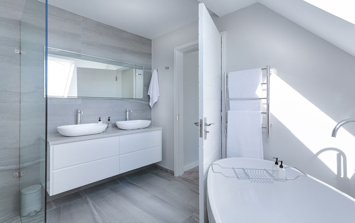 Bright modern bathroom with double vessel sinks, a freestanding bathtub, large mirror, and sleek gray tile flooring.