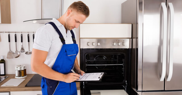Man wearing blue overalls with a clipboard in the kitchen, marking of checklist.