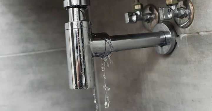 View of leaking pipe with water dripping on it underneath the sink