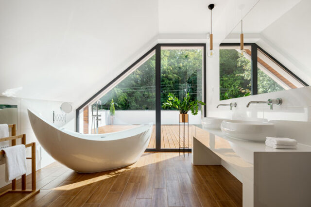 Modern bathrooms with luxurious curved soaking bath with with windows outlooking to green trees.