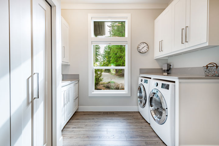 A decent sized room with a window, separate washing machine and dryer on the floor with bench and sink on the opposite wall.