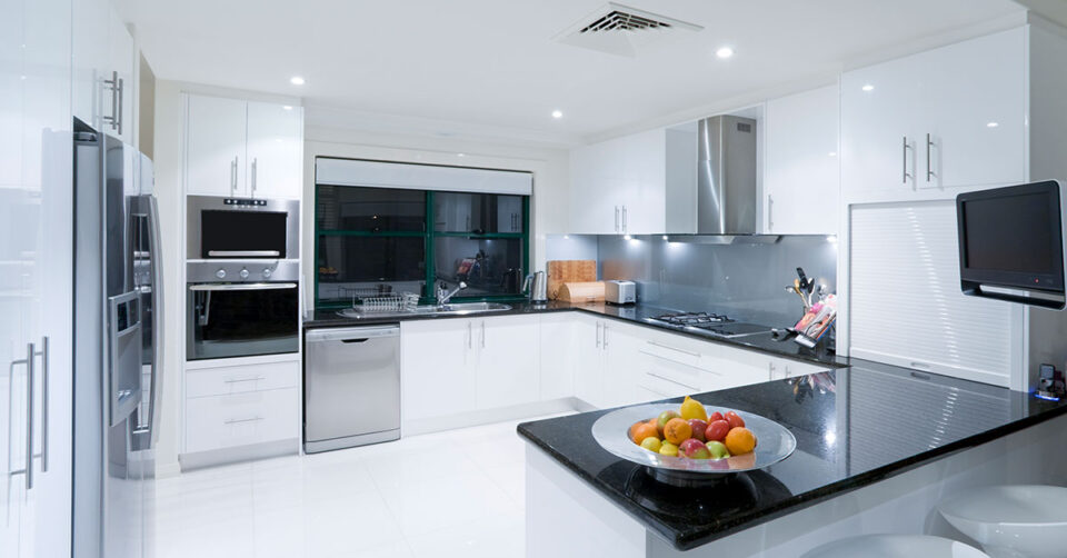 Large spacious modern kitchen with black tabltop, white cabinets and stainless steel appliances.