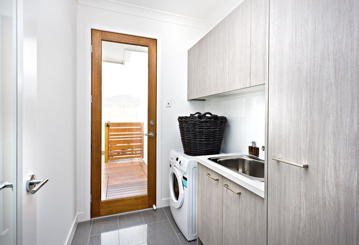 A cleverly placed laundry with a washing machine next to a large sink and cupboards with a door leading to outside.