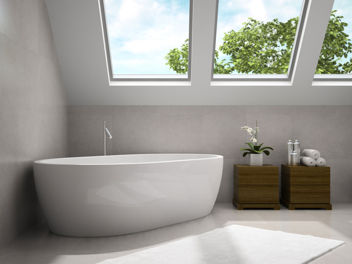 Minimalist bathroom with a freestanding white bathtub beneath large skylights, next to wooden storage units with towels and a plant.