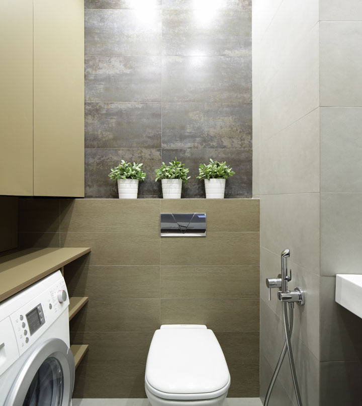 Compact modern bathroom with a wall-mounted toilet, built-in storage, washing machine, and decorative plants on a tiled feature wall.