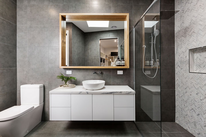 Modern bathroom with dark gray tiles, a white floating vanity, vessel sink, walk-in glass shower, and a large framed mirror.