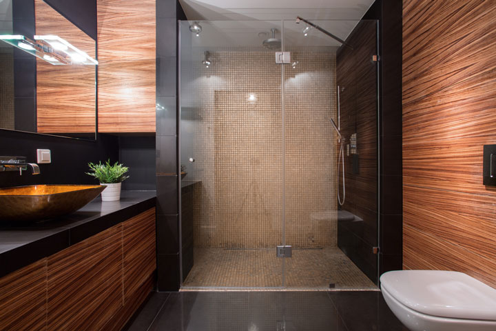 Stylish bathroom with rich wood-textured walls and cabinets, a vessel sink, and a large glass-enclosed shower with mosaic tiles.