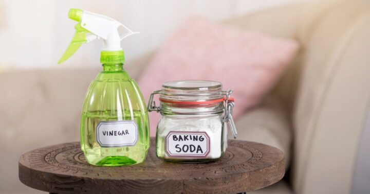 Green spray bottle with labelled with Vinegar and a small glass jar with the label of Baking Soda.
