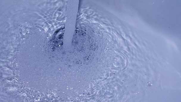 A sink with an open faucet and stock water.